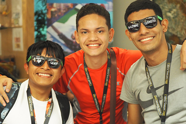 Three students indoors posing together for a group shot wearing lanyards with two wearing sunglasses.