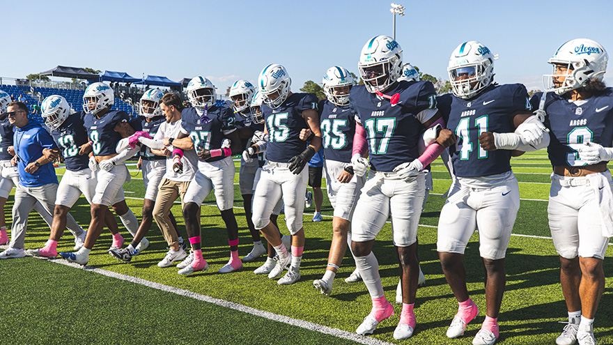 Members of the UWF football team walking in a line on the football with their arms chained together.