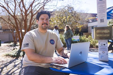Student using a laptop at an outdoor table.