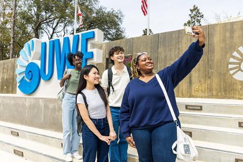 Four students talking a group selfie in front of the UWF nautilus shell outdoor display.