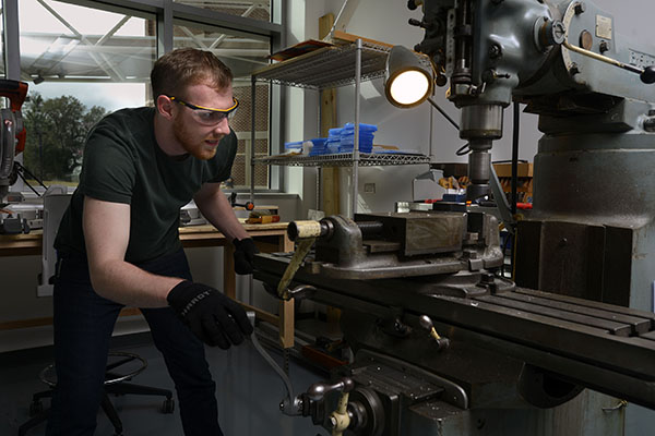 Mechanical engineering student wearing safety glasses and gloves while using a mill machine in a fabrication lab.