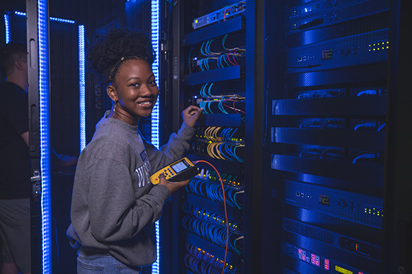 UWF cybersecurity student smiling at camera while working on cybersecurity related computer equipment at the UWF Center for Cybersecurity.